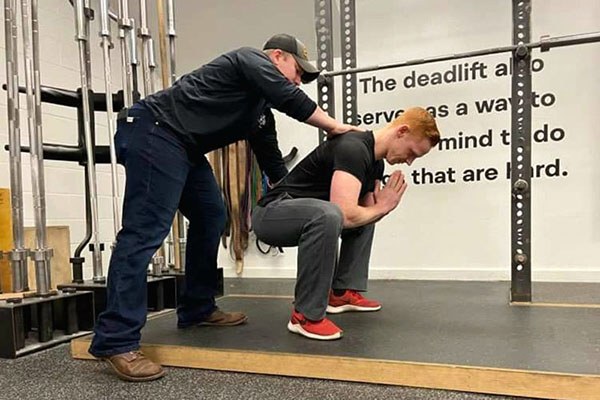 cody annino adjusts back position on a lifter during the teaching method for the squat