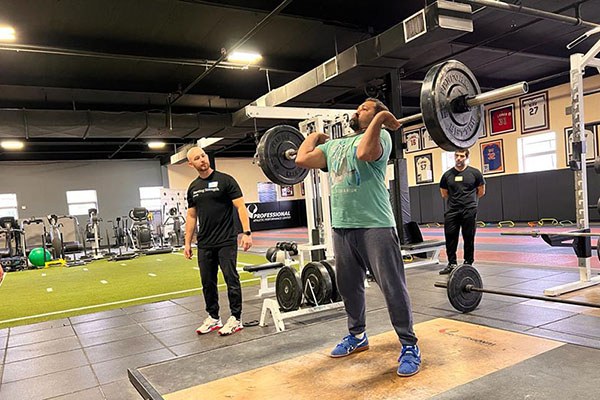 chris coaches kartik through a set of power cleans at a starting strength camp