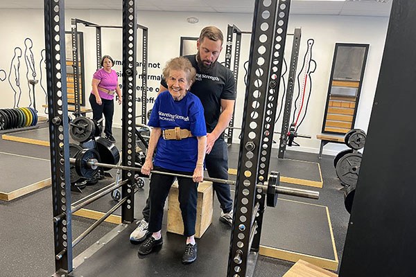 merce smiles as she warms up her rack pulls with chris reis at starting strength cincinnati