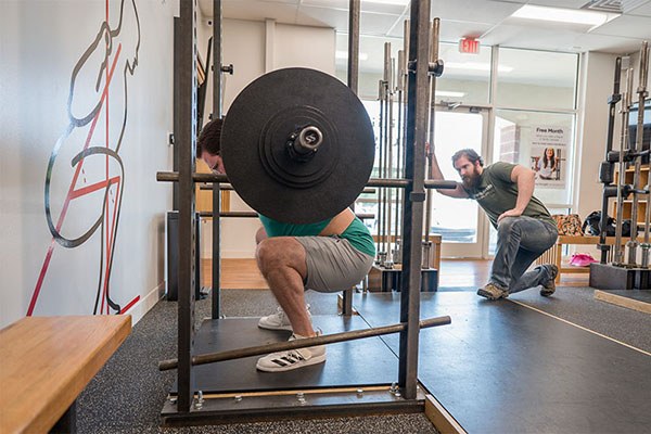 ryan at the bottom of a squat as he is coached by dan buege