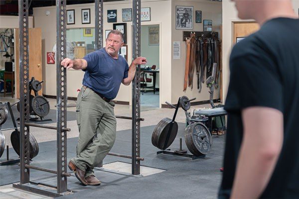 mark rippetoe leaning on a power rack in the gym