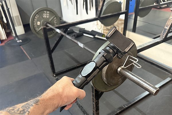 rusty holds a recording stand in front of a rack at the gym